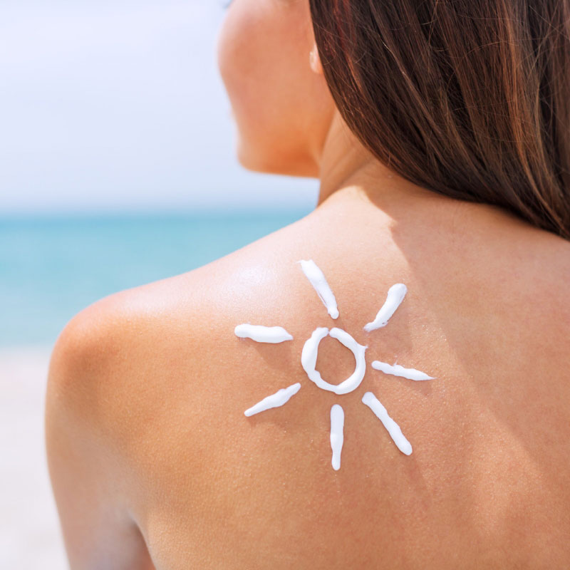 nainen rannalla ja selkään piirretty aurinko aurinkovoiteella