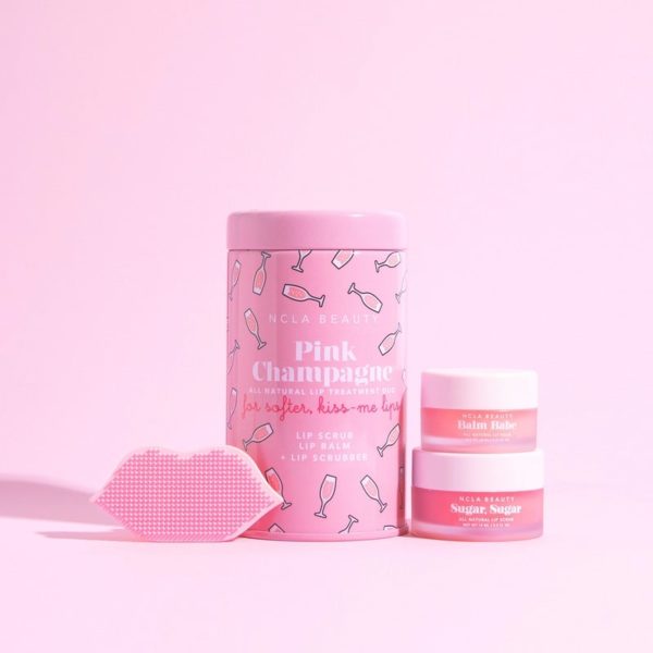 vaaleanpunaisella taustalla pinkki shampanja huultenhoitosetti pakkaus 2 lasipurkkia ja huultenmuotoinen huultenkuorija
