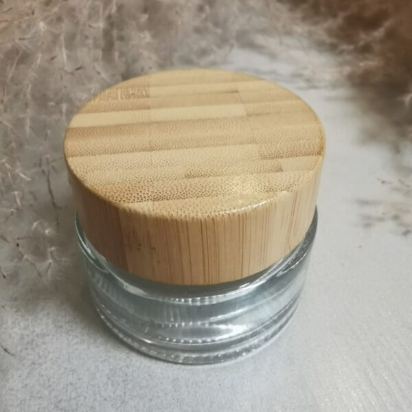 kiskasta lasia oleva tyhjä kosmetiikkapurkki bambukorkilla taustalla heinä